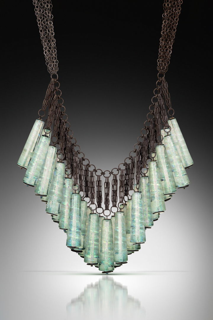 Each component is shaped in the flame using dichroic glass and a graphite paddle. The 30 glass components are then sewn onto hand-fabricated  oxidized sterling silver frame.