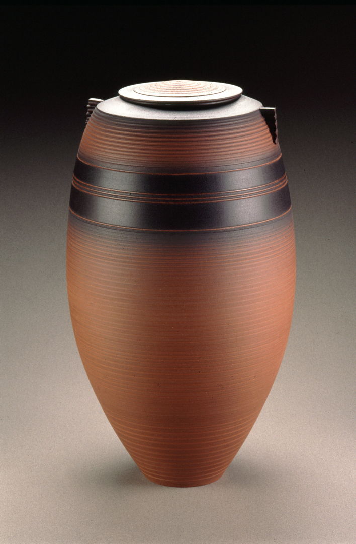 Thrown brown terracotta pot with black accents, lid, and small triangular handles.