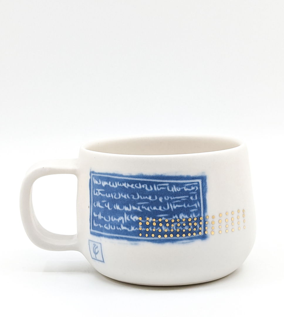 White mug accented with gold dots and blue persian writing.
