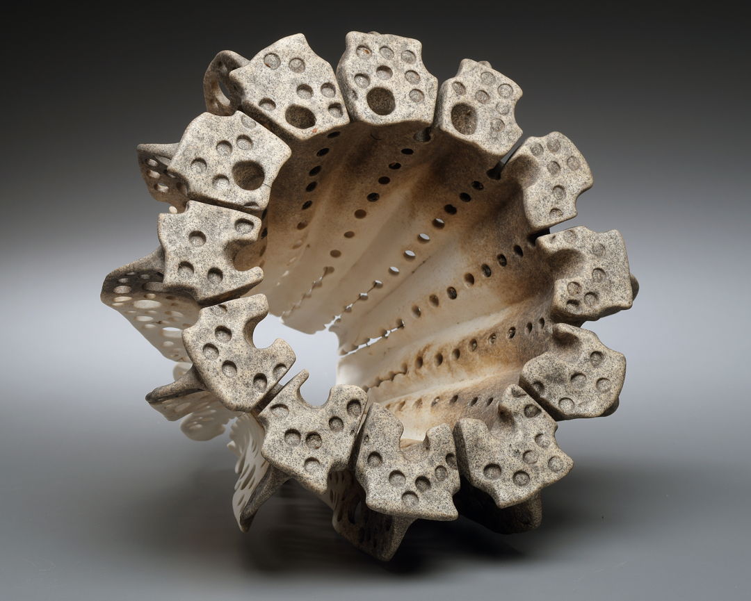 Organic hollow porcelain form with grimy surface accenting the many circular indents covering the piece.