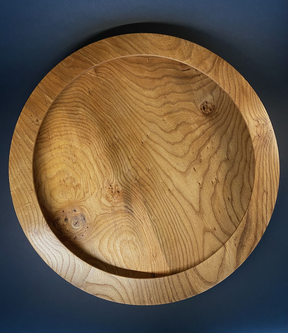 A huge slab of Elm is hard to find. This surface could be plain and simple. But by giving the platter an unusual undercut rim the grain is accentuated and interest is heightened overall. Can be hung or placed on a large table.