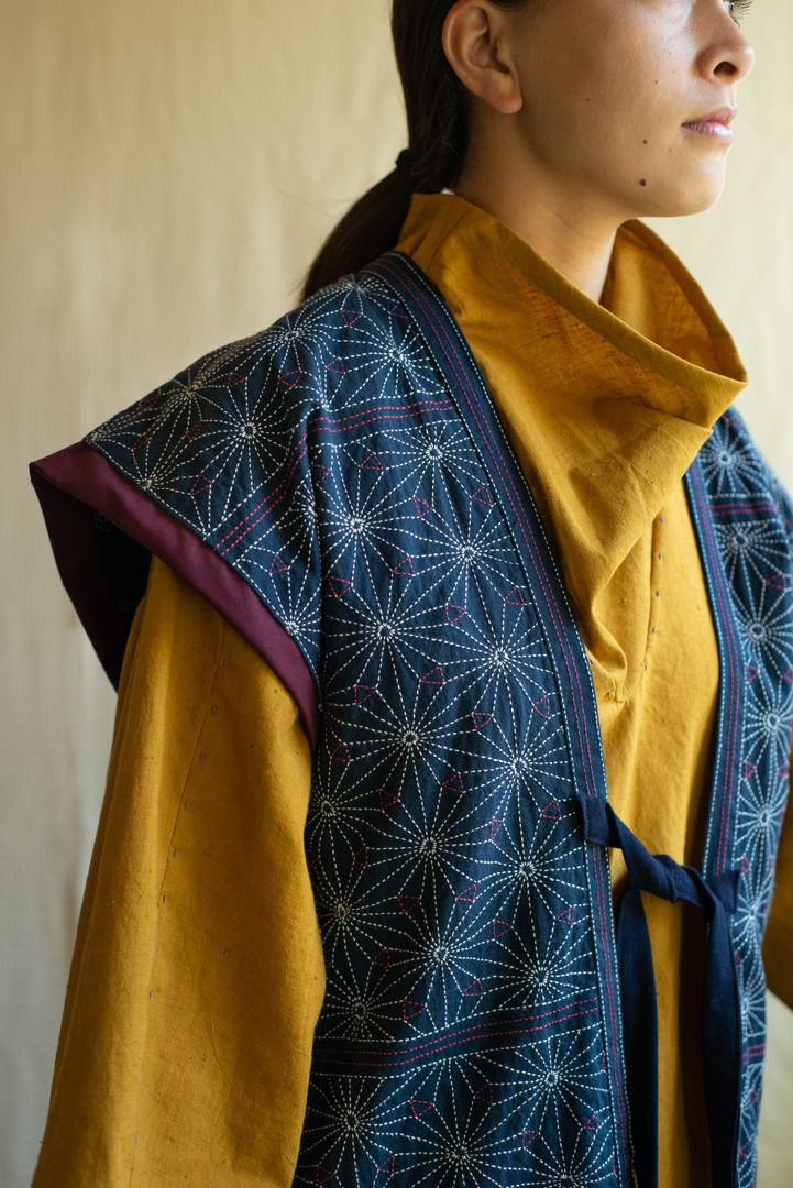 The vest features a star-like flower pattern  hand-stitched on hand-dyed indigo cotton fabric. The brightness and depth of the tunic brings out the strength of the flower stitch. The tunic exhibits hand-stitched designs on natural cotton fabric hand-dyed with turmeric plant.