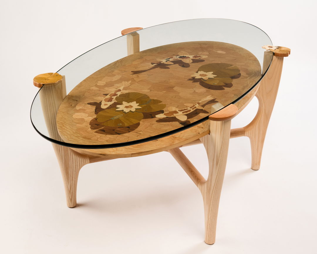 The koi pond within this table is a work of marquetry. Each piece of wood is cut by hand and fitted to create the image. I use the double-bevel technique to obtain fine detail. (Ash  ash burl  walnut  butternut  holly  laurel burl  mahogany  ebony  and dyed poplar)