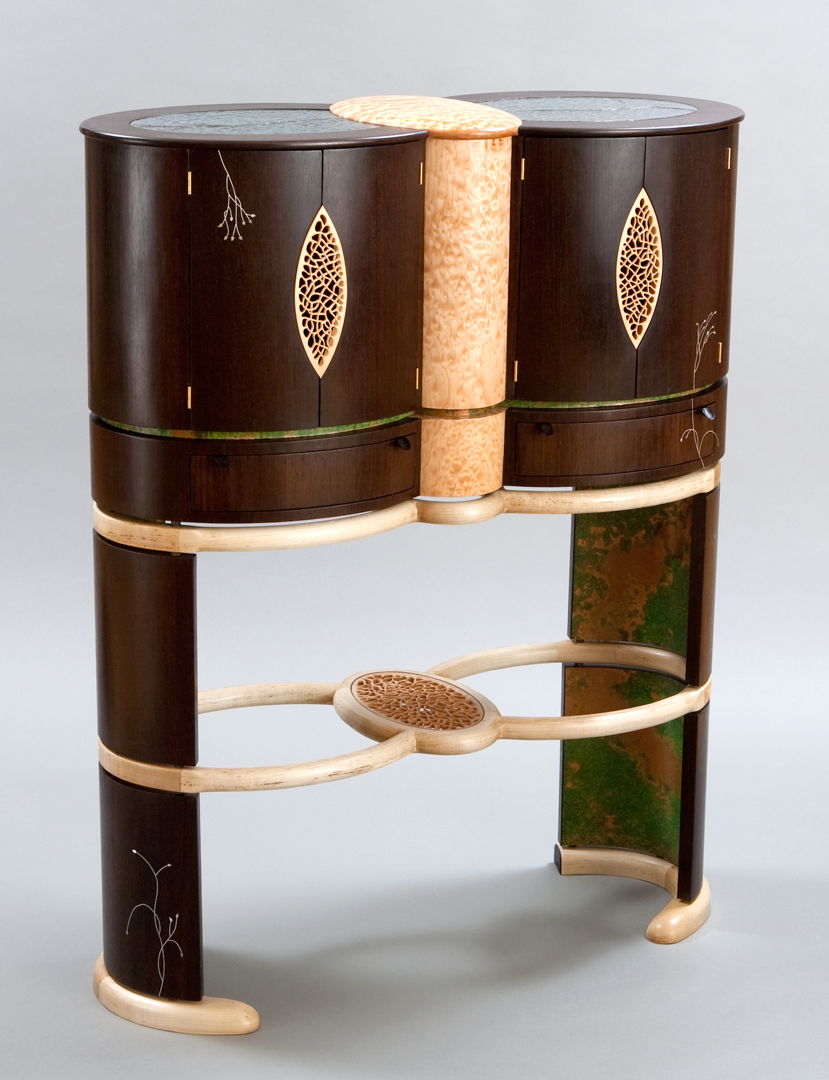 Abraxas features twin oval wenge cabinets joined by a third intersecting blistered maple oval. There are pierced doors  a patinated copper interior  a copper foiled glass top and inlay embellishment of sterling silver (engraved with William Blake poetry)  abalone and mother of pearl.