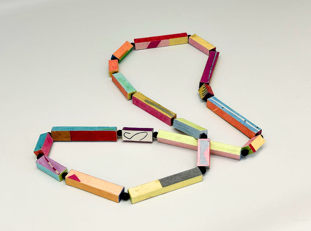 Pipage Necklace is composed of many rectangular-shaped pipes  each pipe a different length with different colors and patterns on each side and both ends. The little pipes are made from layered mat board. Colors and patterns are added using layers of papers “painted” on with brush and glue. The colorful pipes are linked with cord  with small black beads in between each one. The Pipage Necklace is sealed for wear  and comes as a single strand as seen here  as double strands  and earrings.