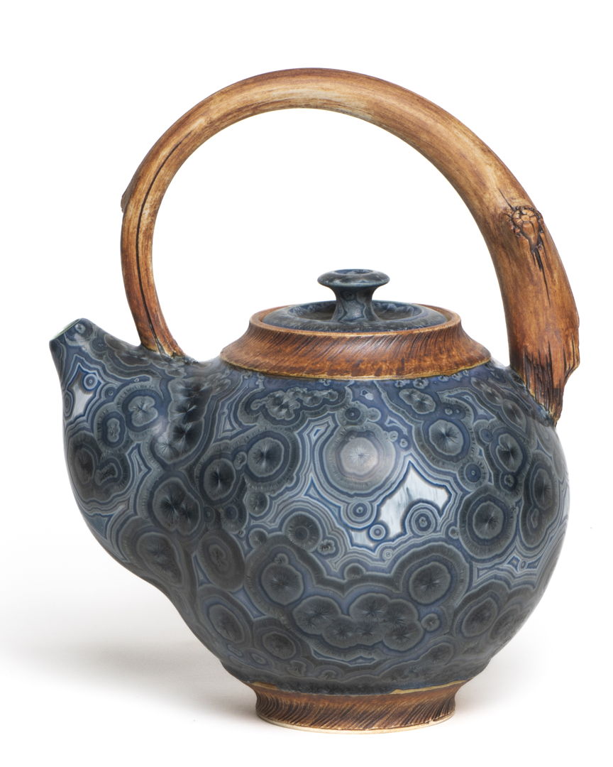 Teapot with crystalline glaze body and handle and base made to look like wood.
