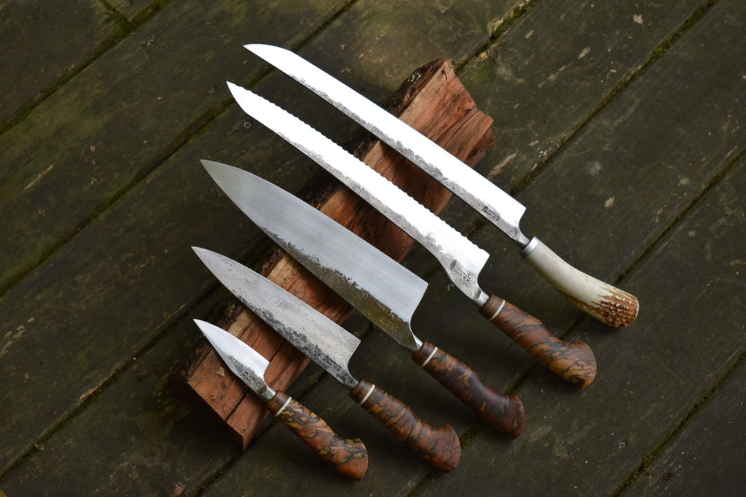 Five piece knife set consisting of paring  petty (utility)  chef  offset bread  and slicer. Matching handles of bocote  ivory G10  and spalted maple. The spalted maple is from my father's farm in Baltimore County  MD. The slicer has a deer antler that came from a whitetail deer shed that was found by my father in Anne Arundel County  MD. The utility knife has a laminated steel blade  with a wrought iron jacket. The wrought iron came from Amish Country in PA.