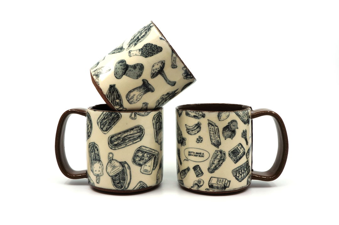 Three mugs, one with illustrations of mushrooms, one with illustrations of canned fish, and one with illustrations of various groceries.