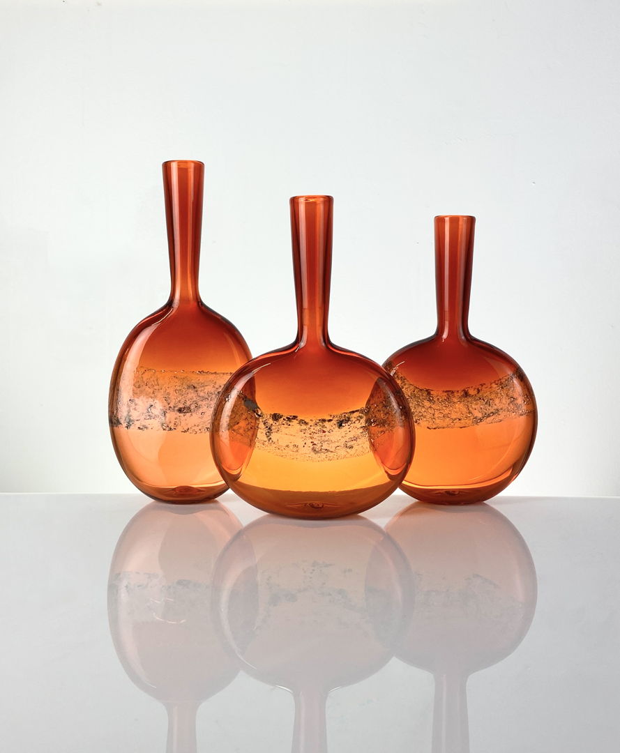 These vessels are created with an optical band of copper foil that when reacted with the glass  turns a bubbly blueish tone. We also create these handblown bottles with silver foil in the same painterly application that turns a beautiful goldish/blue tone.