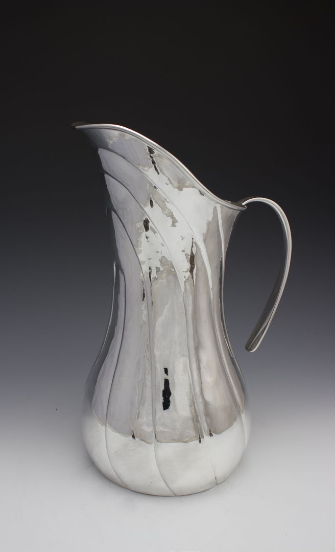 This large statement pitcher or ewer is hand raised from a single sheet of sterling silver. This swooping lines are chased in to big movement and grace to the form.