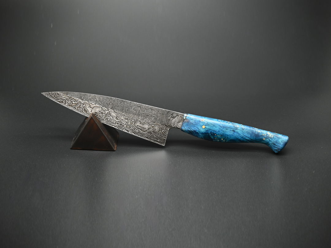An everyday kitchen workhorse  this 7" chef knife's blade is handforged from folded nickel and carbon Damascus steel  mounted on a dyed and stabilized box elder maple handle.