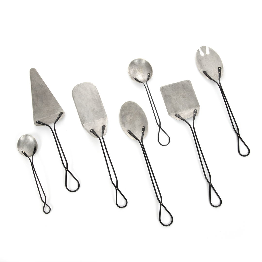 The Foliage Wares Serving Set include a variety of spoons  spatulas  and cake and pie servers. Dimensions vary  with the largest pieces measuring 3" wide x 14" long. Shown with photo-etch fern motifs on tinned brass with blackened stainless handles  attached with German silver rivets.