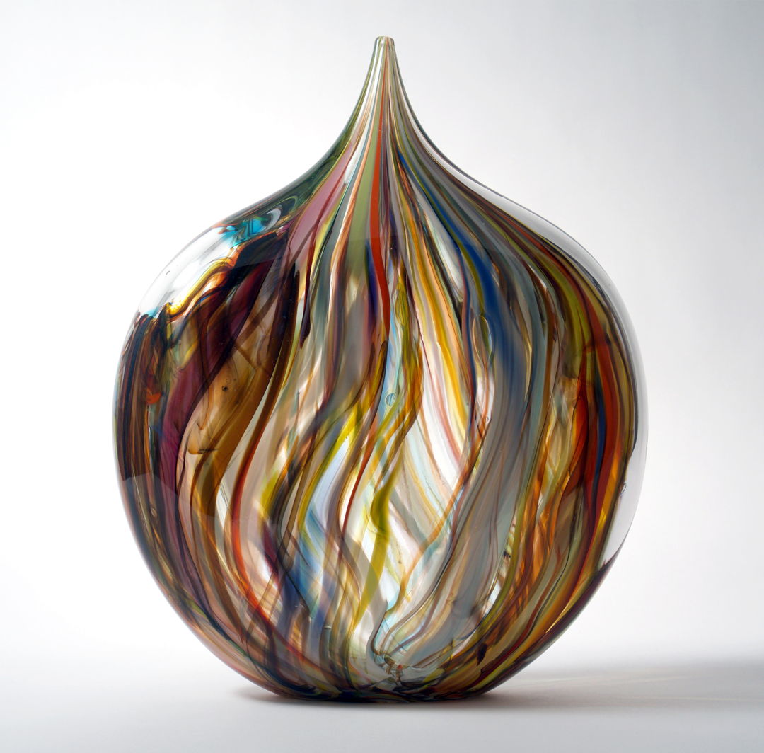 Blown glass form with painterly streaks of color that draw a heart shaped form. Randomly placed windows of clear glass magnify areas of the lively pattern. The vibrant array of colors remind us of a fresh box of crayons.