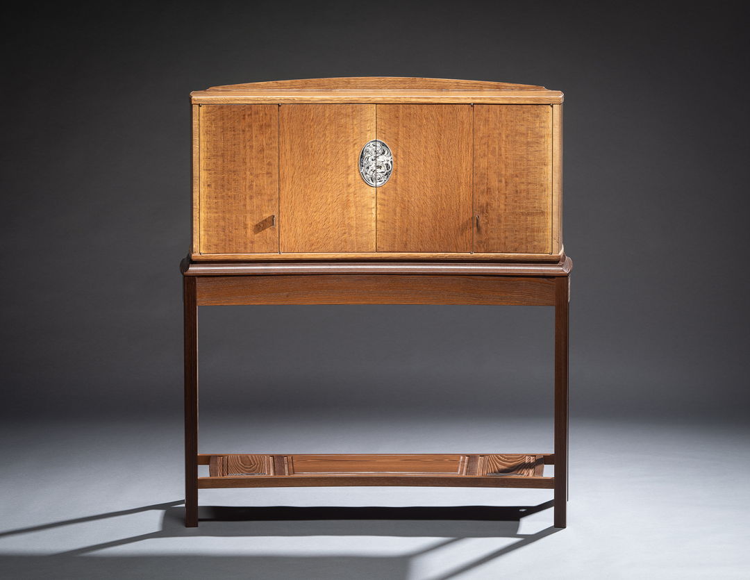 This cabinet features figured English brown oak and a stand of torrified ash. The engraved nickel silver escutcheon plate opens to reveal a detailed interior of holly and ash. In dramatic contrast to the rich tones of the exterior  these naturally light woods illuminate the cabinet from within.