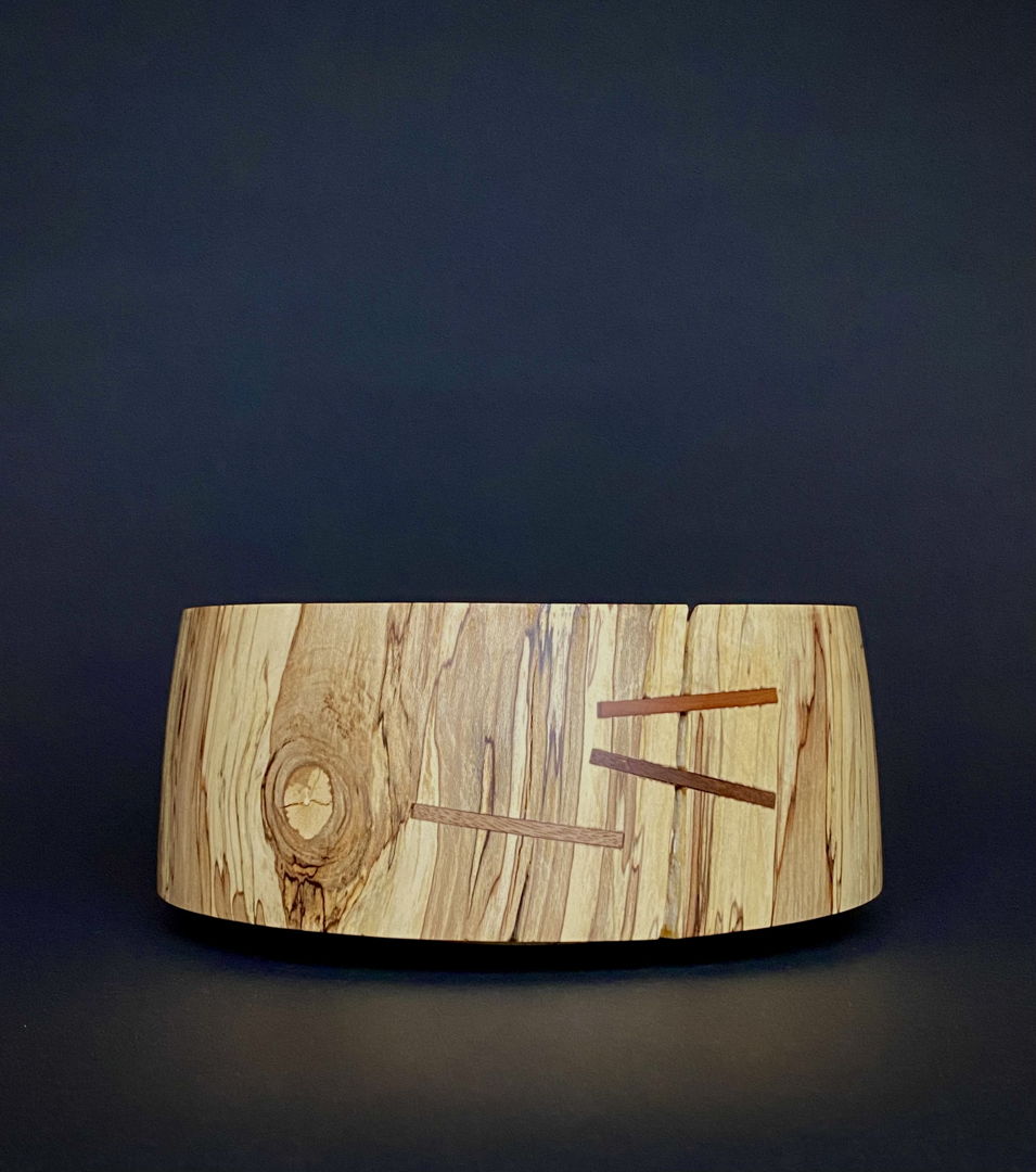 A straight sided bowl with colors sliding down the sides. Ties of Cherry and Walnut bind the cracks.