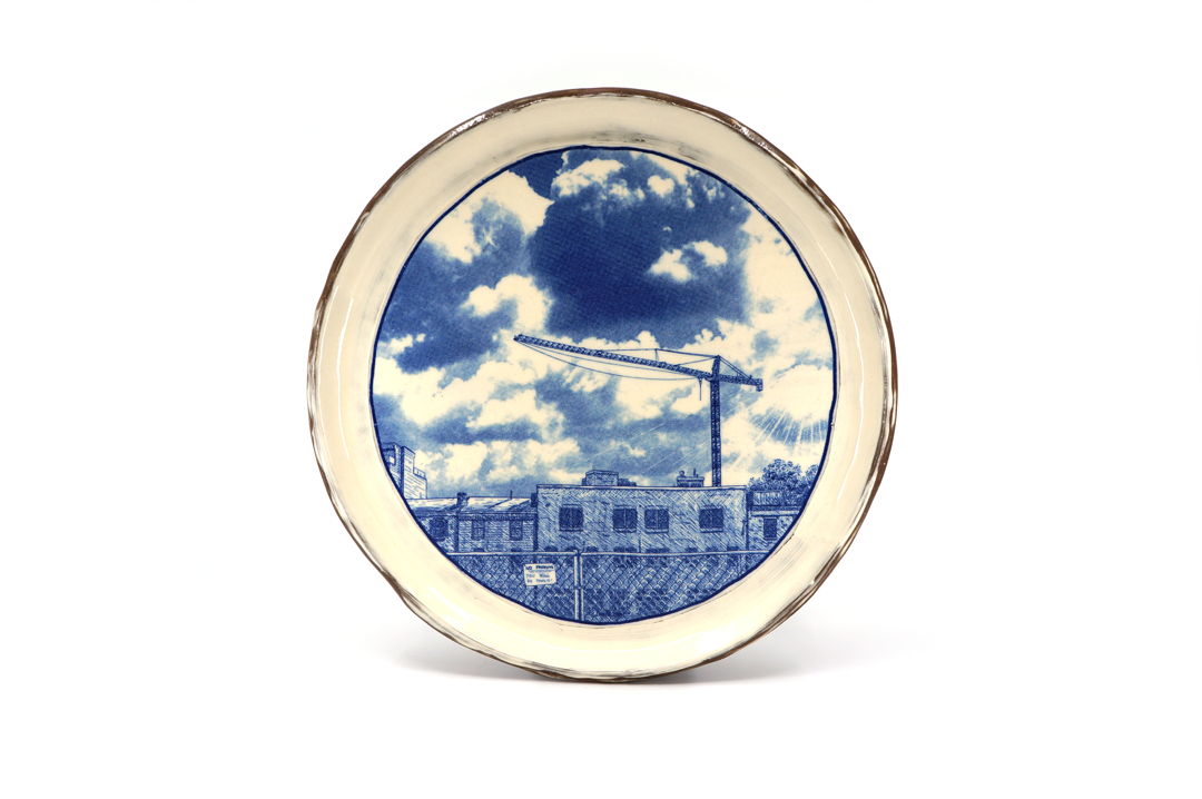 ceramic plate with blue and white picture of a fenced off property and construction crane.