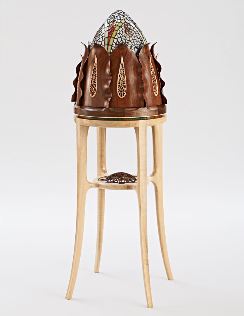 This presentation cabinet has 8 sculpted walnut leaves that all open in unison to reveal a glass dome that rotates to find doors that access the interior. It features delicate carving  piercing  and inlays of silver  mother of pearl  and abalone. Inspired by succulent plants.