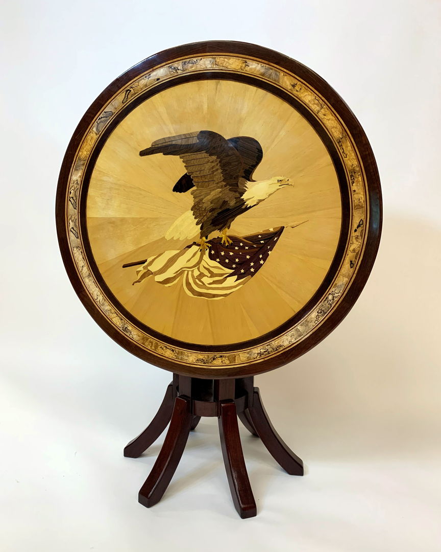 A stunning marquetry image of a bald eagle adorns this tip table. The tabletop is made from hand-cut wood pieces in natural colors with no stains or dyes used. (purpleheart  spalted maple  hemlock  and a variety of natural woods create the image)