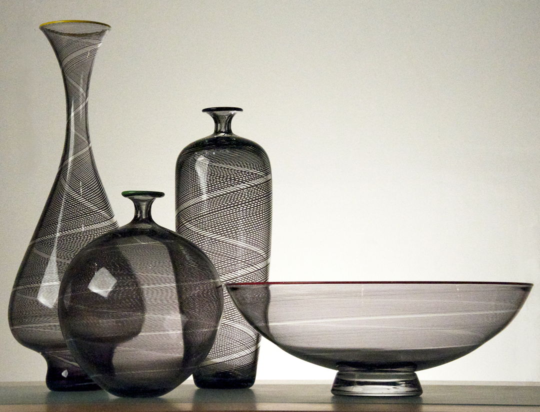 Blown Glass vessels made from clear glass with fused black canes or rods of black glass melted into the surface and twisted while blown. Each piece is finished with a red colored glass lip.