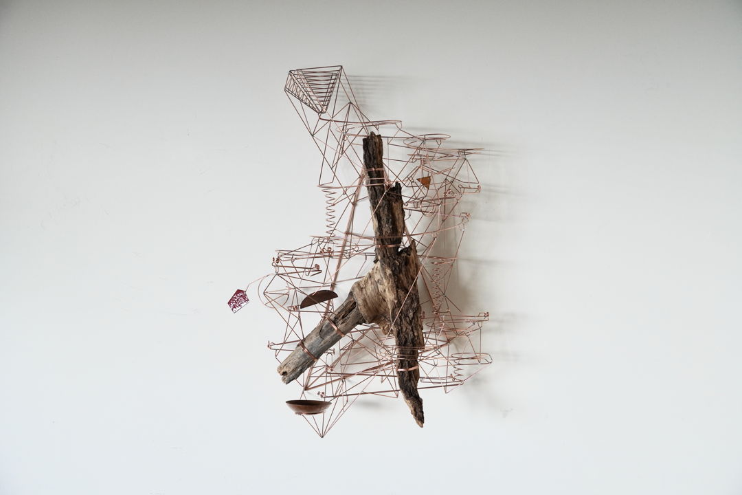 Wall-mounted copper wire and wood kinetic sculpture. To activate  steel marbles can be dropped into the top of the sculpture. The marbles roll down the track which splits and dumps the balls into the copper bowl. kiln-fired enamelled copper and sheetmetal make up part of the interactive elements.