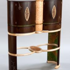  Abraxas features twin oval wenge cabinets joined by a third intersecting blistered maple oval. There are pierced doors  a patinated copper interior  a copper foiled glass top and inlay embellishment of sterling silver (engraved with William Blake poetry)  abalone and mother of pearl.