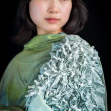 The gray-ish green tones  reminiscent of shadows at the bottom of the sea  sparkle vividly in the flickering wind and glistening sunlight. The blend of silk and cotton fabric creates a beautiful layering of colors  producing complex sparkles with each drape. The combination of this fabric and the shibori dyeing technique adds a unique surprise and complexity to the beauty of the shawl.