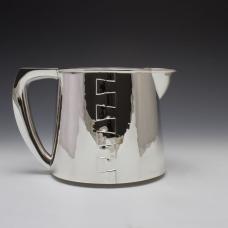 An elegant silver creamer with a constructed design that features a dovetail seam up either side of the piece and flowing hollow handle.