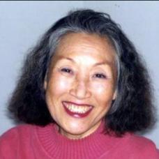 Female with shoulder length black hair and a pink sweater is smiling at the camera